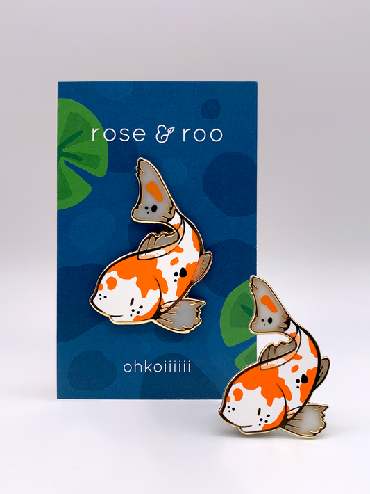 Two Ohkoiiiiii Fish enamel pins in orange, white, and black.