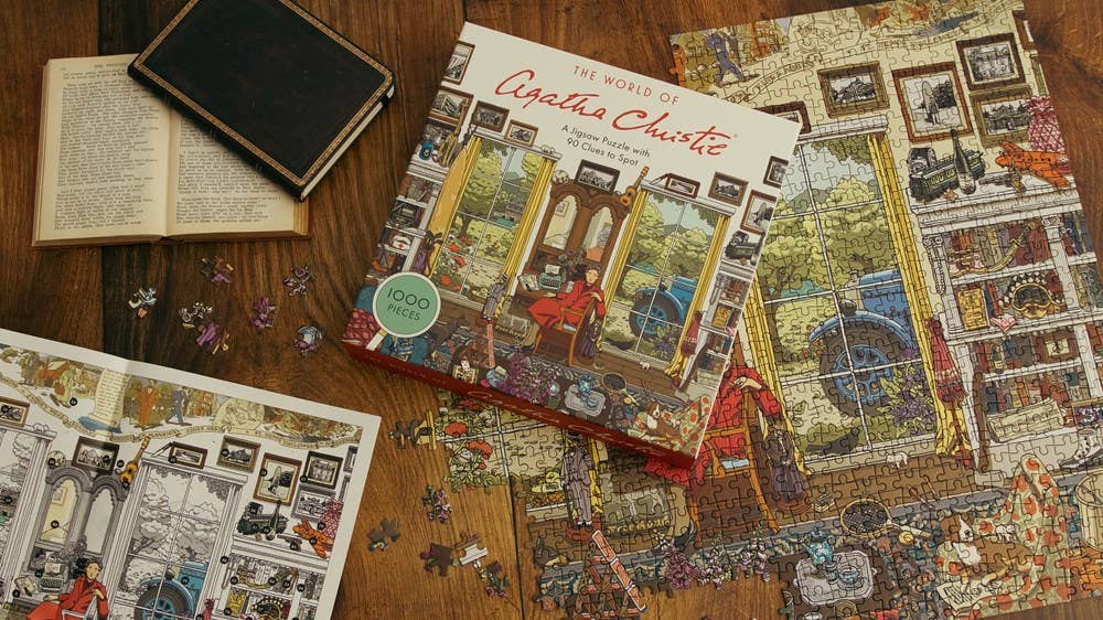 The World of Agatha Christie 1000 Piece Puzzle with box, book, and pieces on a wooden table.