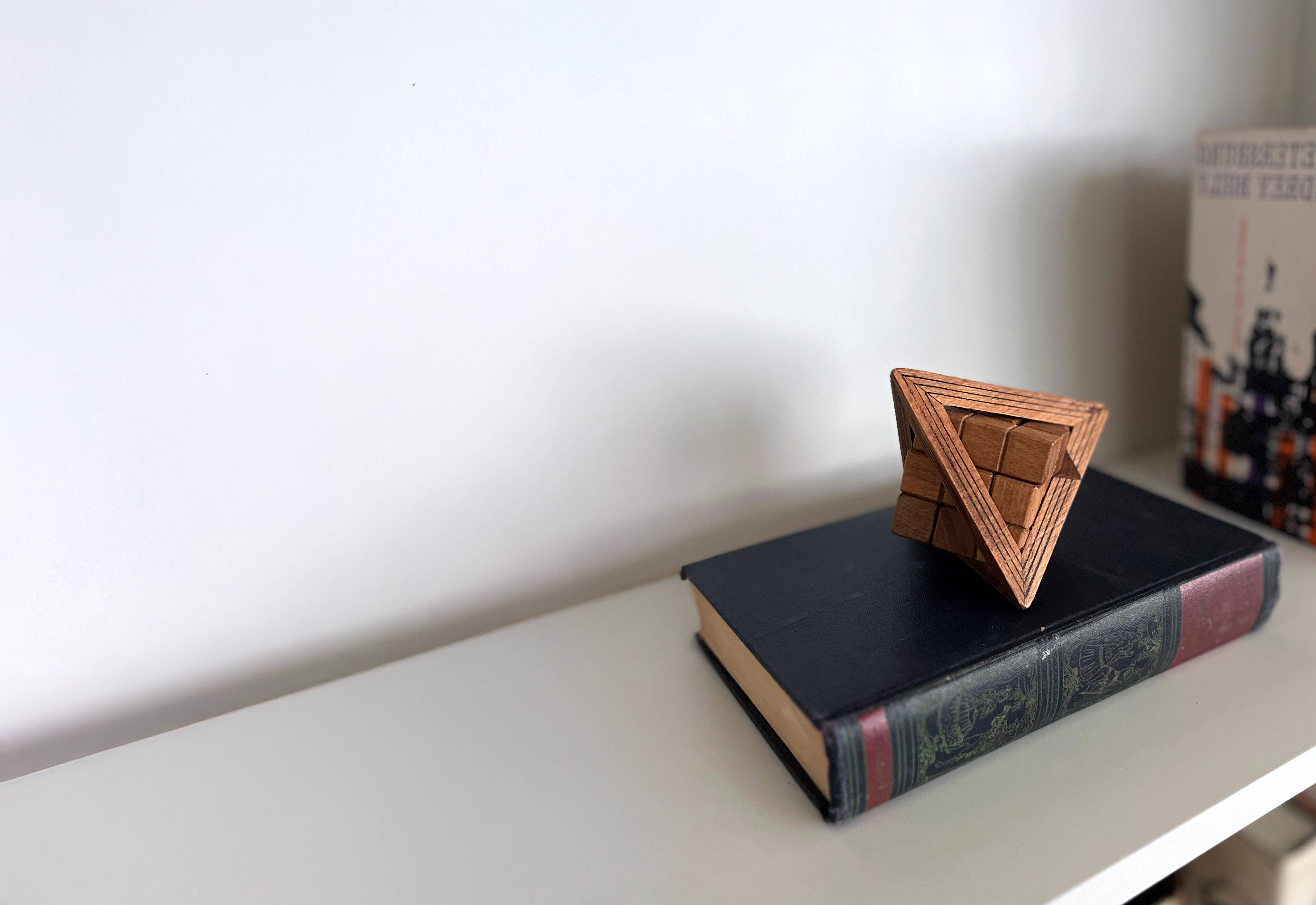 True Genius Egyptian Triglyph Puzzle on a closed book with another book blurred in the background.