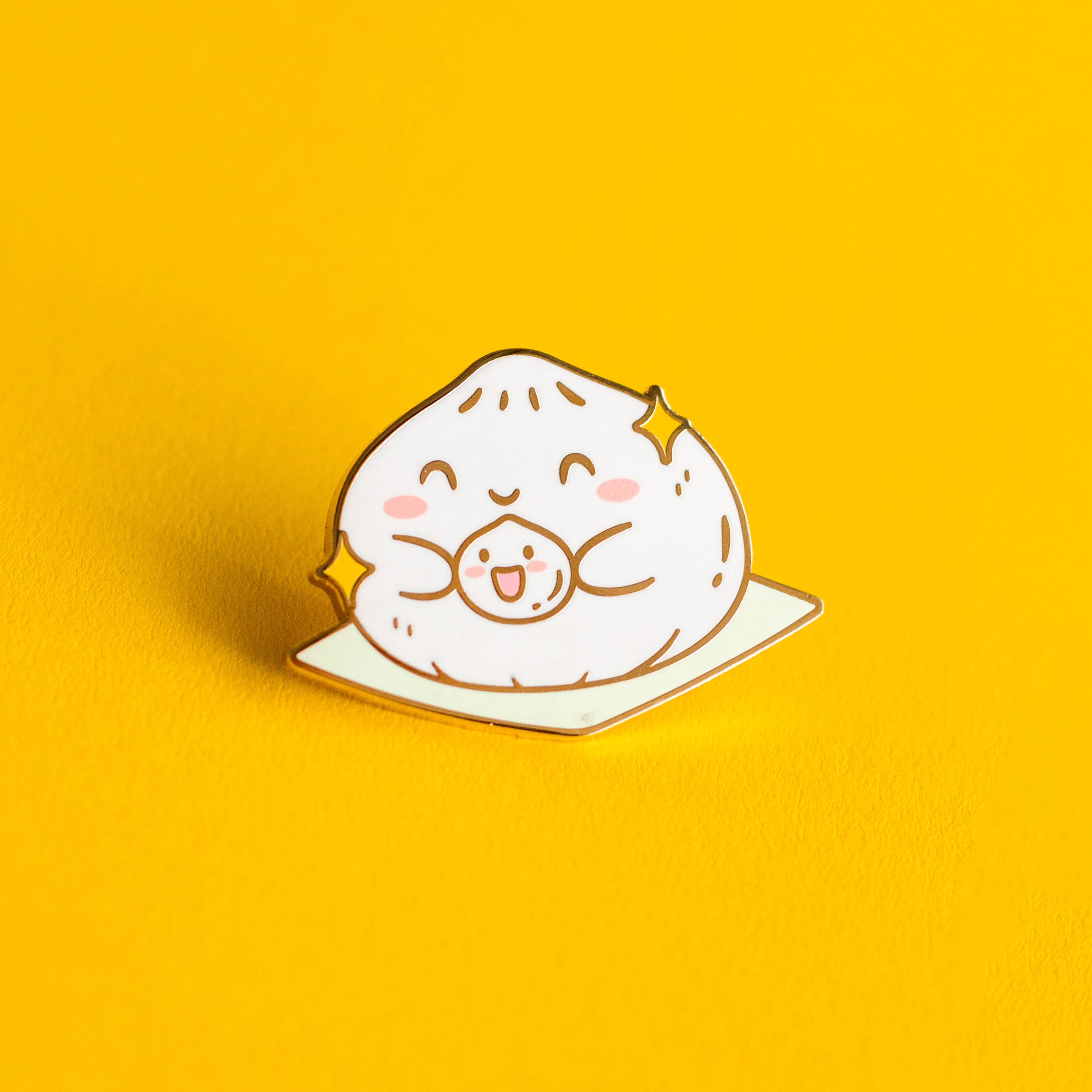 Big and Little Baos Enamel Pin showing two smiling dumplings with sparkles on a yellow background.