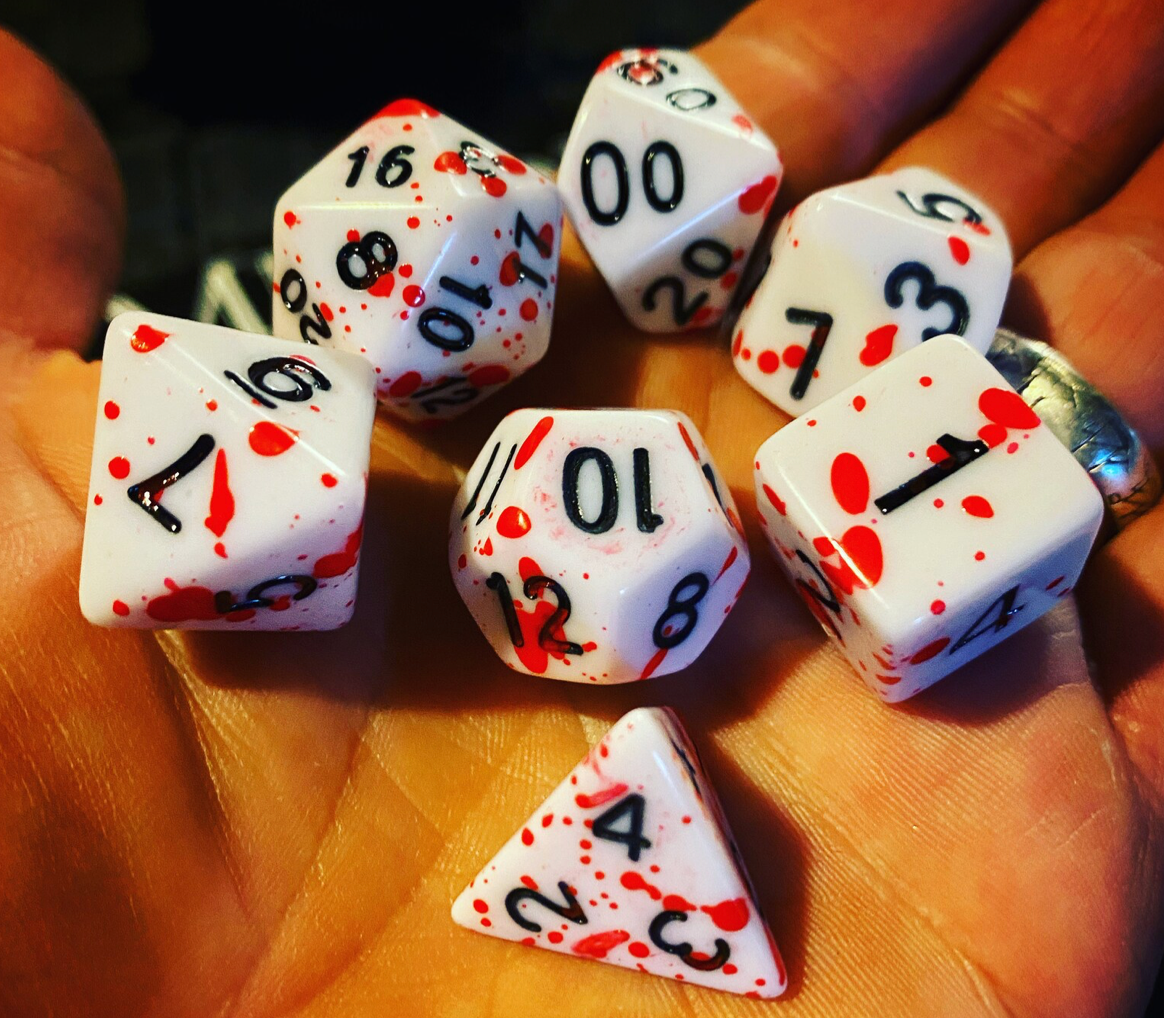 Bloody Dice Set: seven white dice with red splatters and black numbers held in a hand.