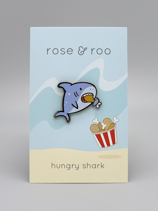 Hungry Shark enamel pin showing a black nickel cartoon shark eating chicken. Card backing with chicken bucket visible.