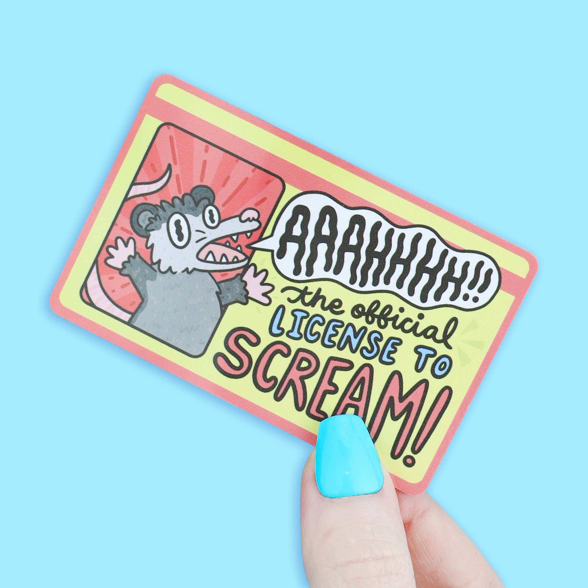 License to Scream Anxiety Fake ID card with cartoon possum and text, held by a blue-nailed hand.