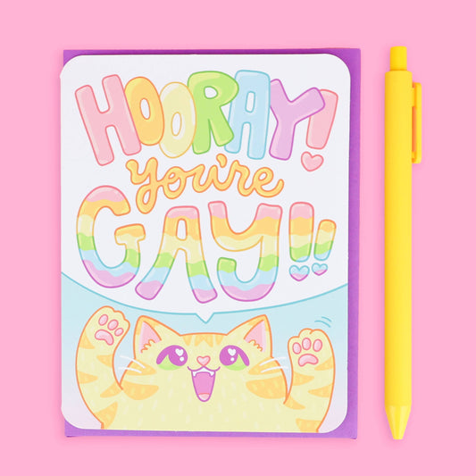 Hooray You’re Gay Kitten LGBTQ Queer greeting card with envelope, pink background, smiling cat, vibrant colors.