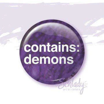 Round purple 1.25 button pin with white text reading demons.