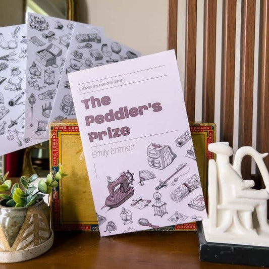 The Peddler’s Prize GM-less RPG game box and two instruction sheets with line-drawn illustrations.