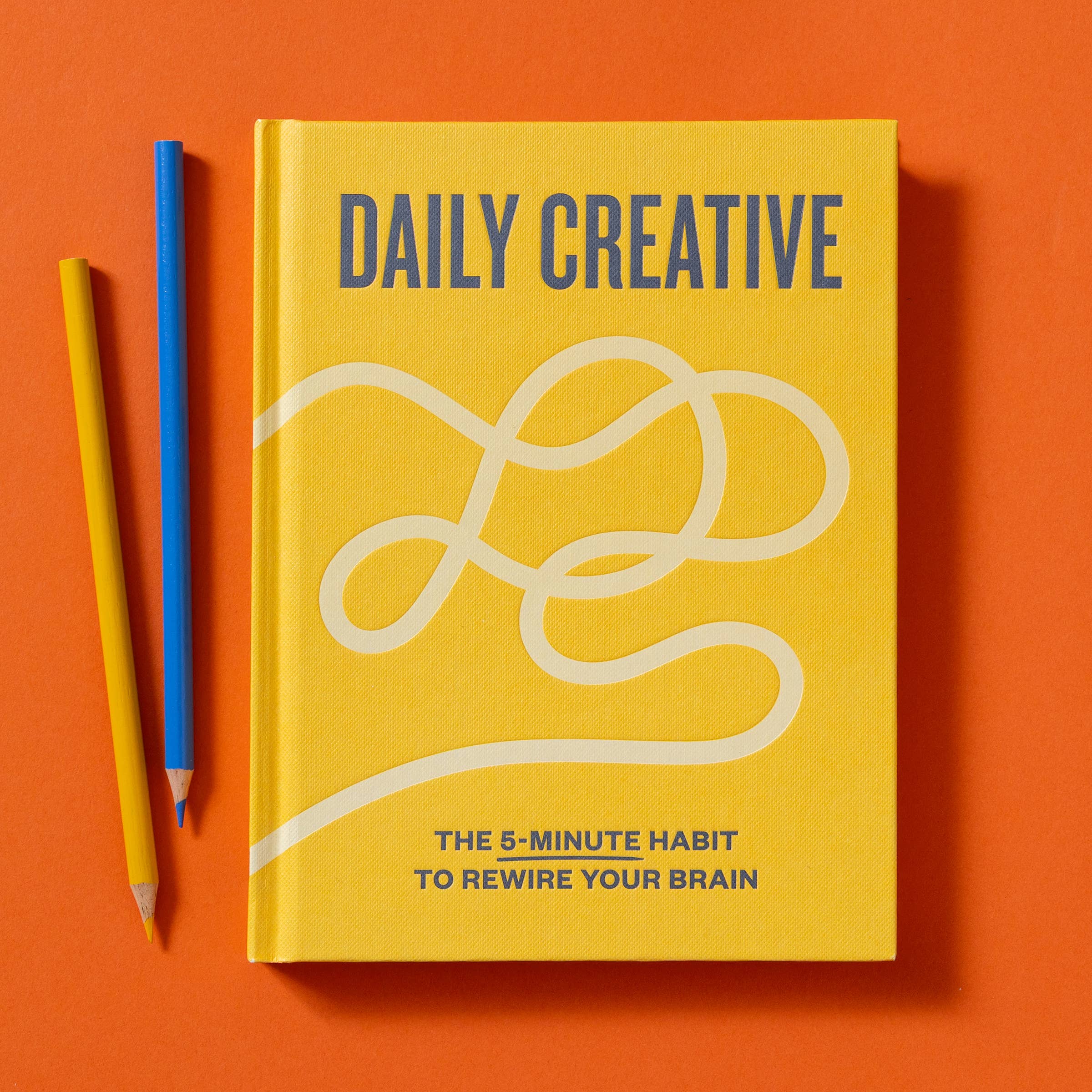 Daily Creative book and two pencils on an orange background.
