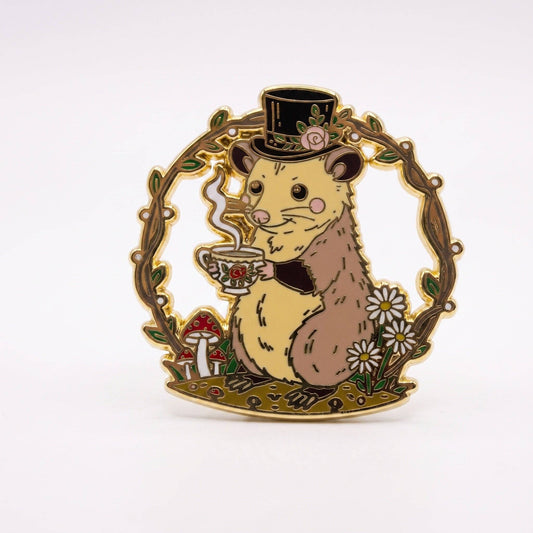 Mr. Fancy Possum hard enamel pin, featuring a possum in a top hat holding a teacup, framed by gold-plated floral branches.