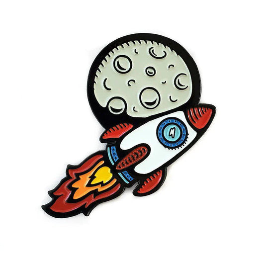 Kolorspun Pins To The Moon Rocketship enamel pin featuring a cartoon rocket flying past a cratered moon.