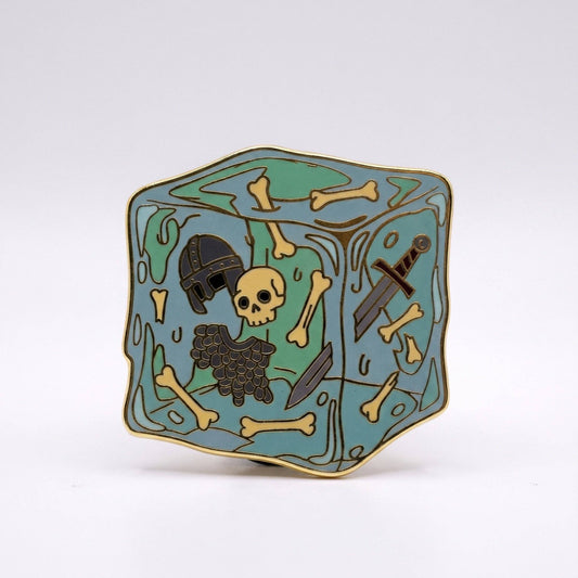 Gelatinous Cube enamel pin: gold-plated, featuring a skull, helmet, and sword inside a translucent blue resin cube.