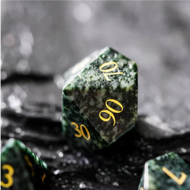 The Algal Gemstone engraved gold ten-sided die by Foam Brain Games on a dark textured surface.