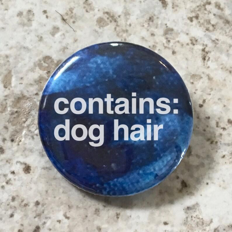Round blue 1.25 button pin with contains: dog hair in white text on a speckled background.