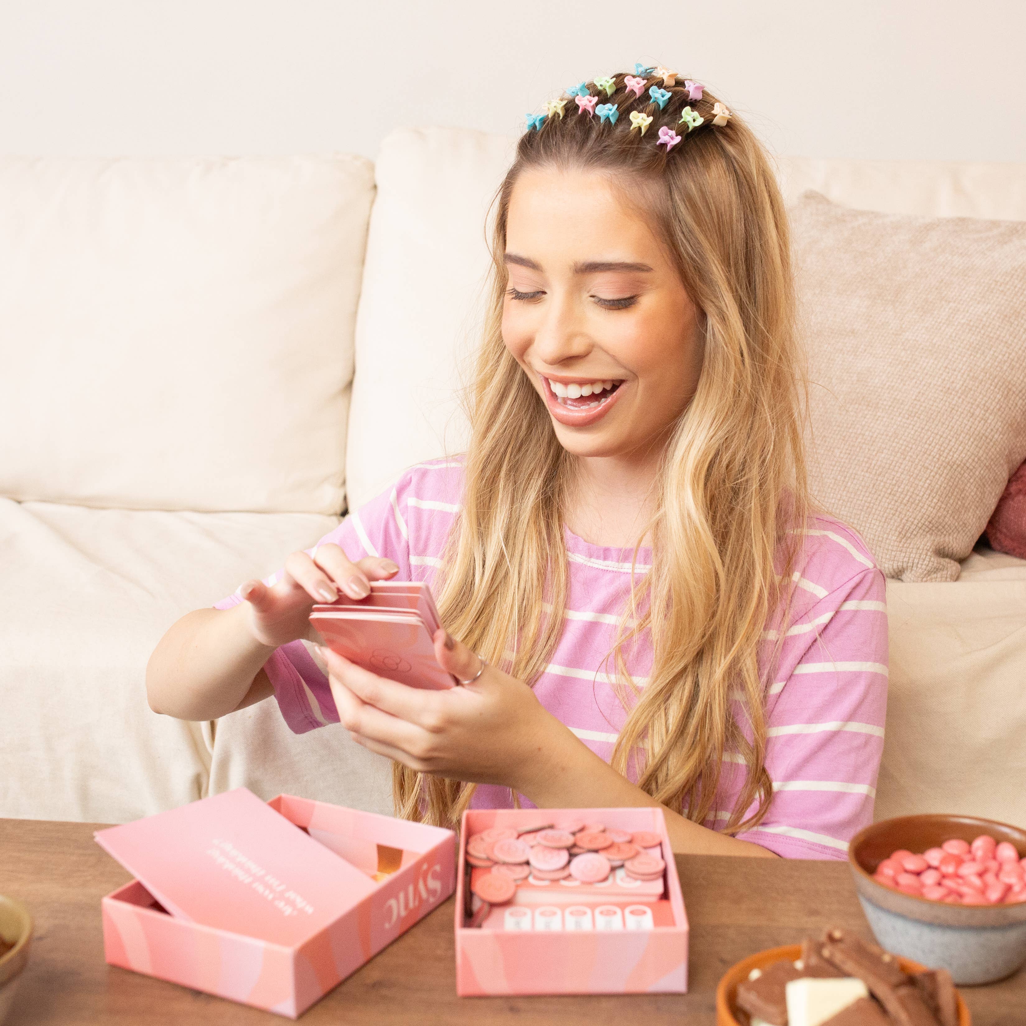 Sync party game being opened by a woman at a table with snacks and candies.