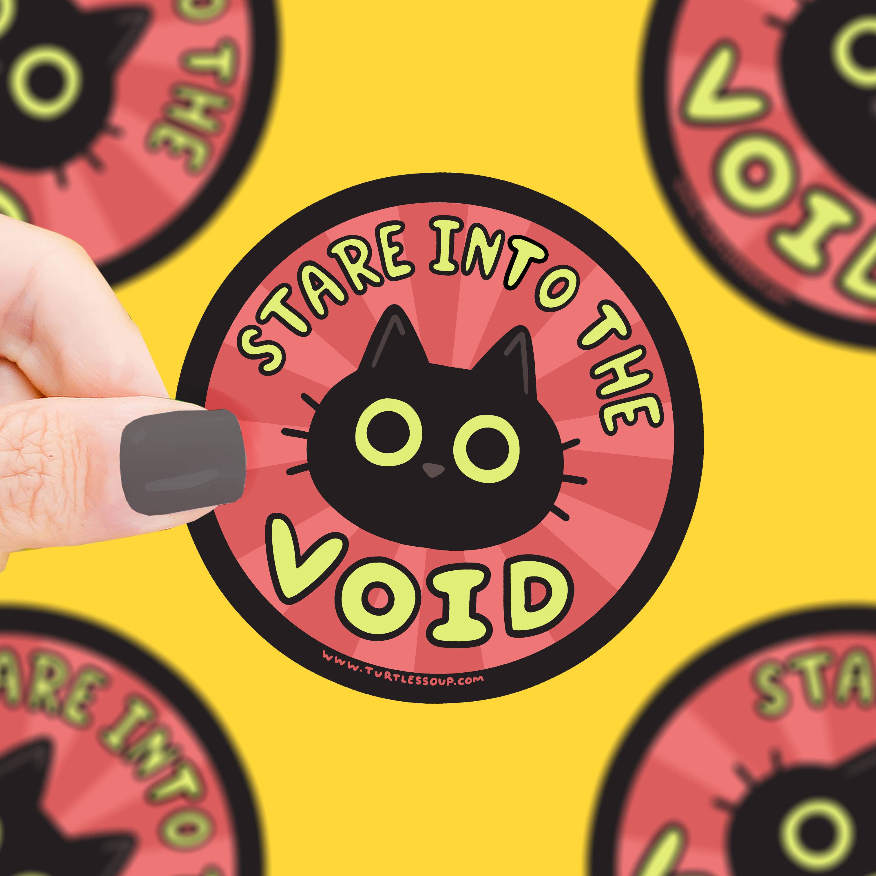 Stare Into The Void Black Cat Kitty Vinyl Sticker by Turtles Soup, red and yellow with cat design, held in a hand.