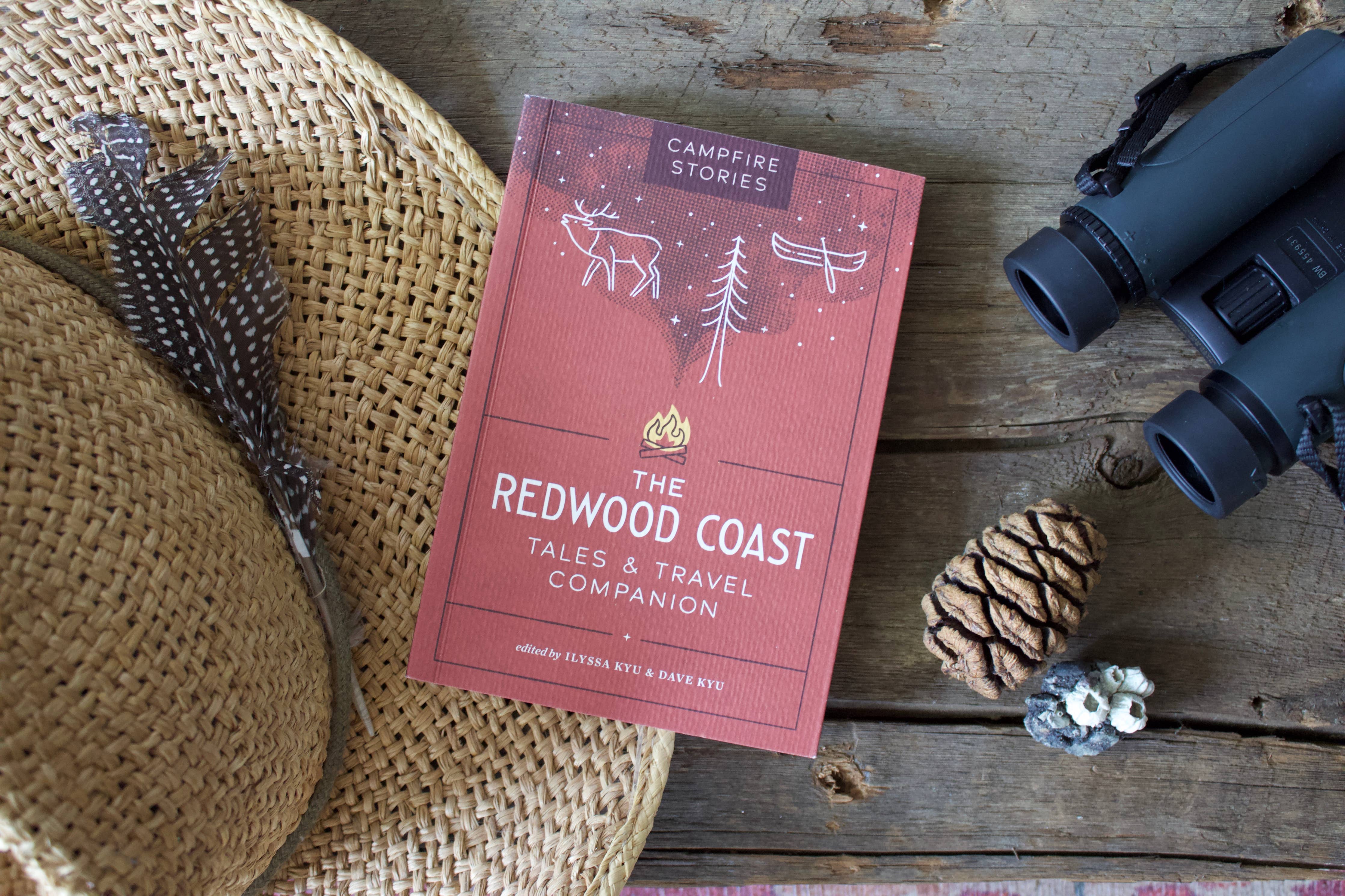 Campfire Stories: The Redwood Coast on a wooden table with a hat, feather, and binoculars nearby.