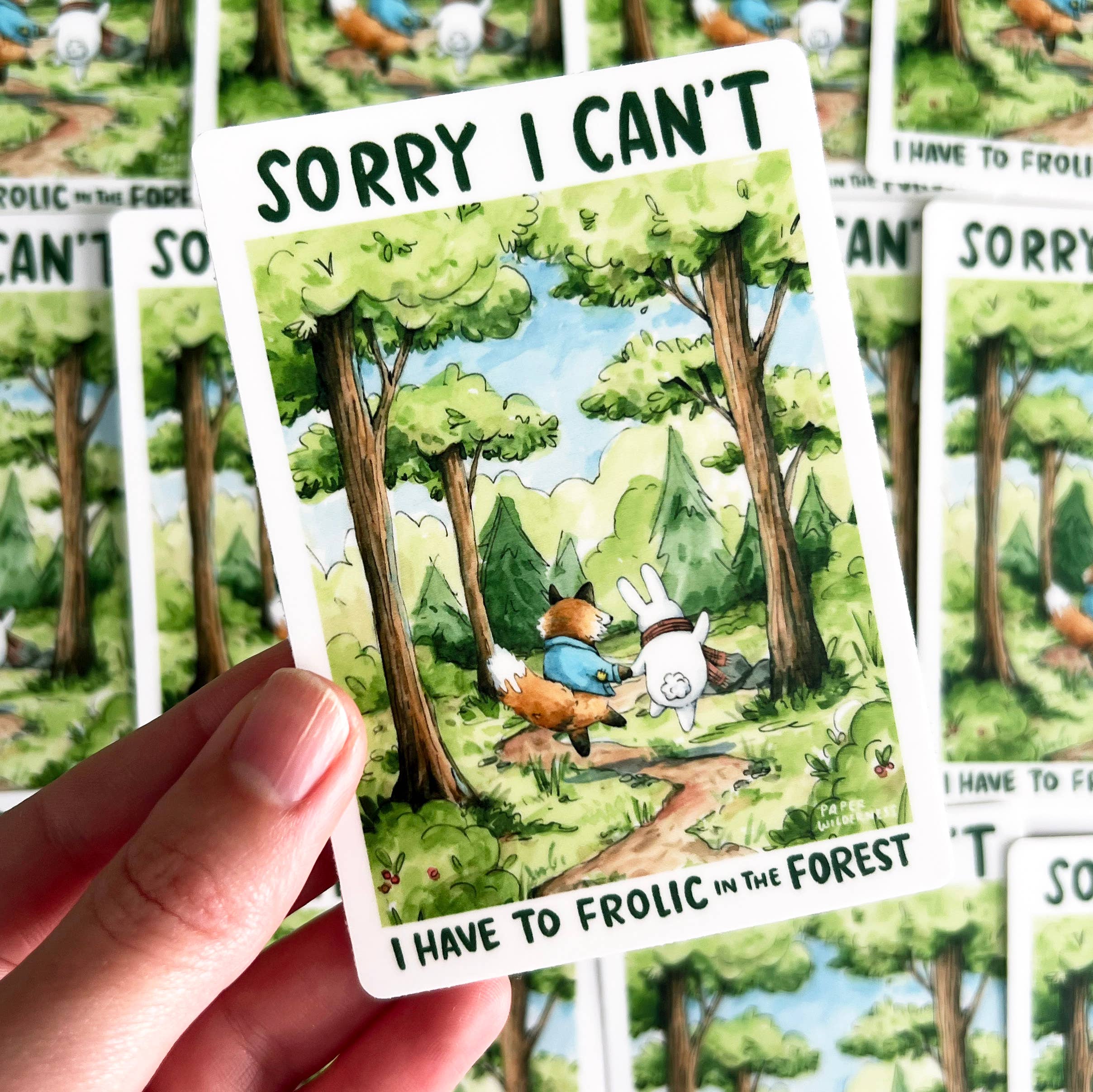 Sorry I Cant I Have To Frolic In The Forest sticker featuring a fox and bunny held on a card by a hand.