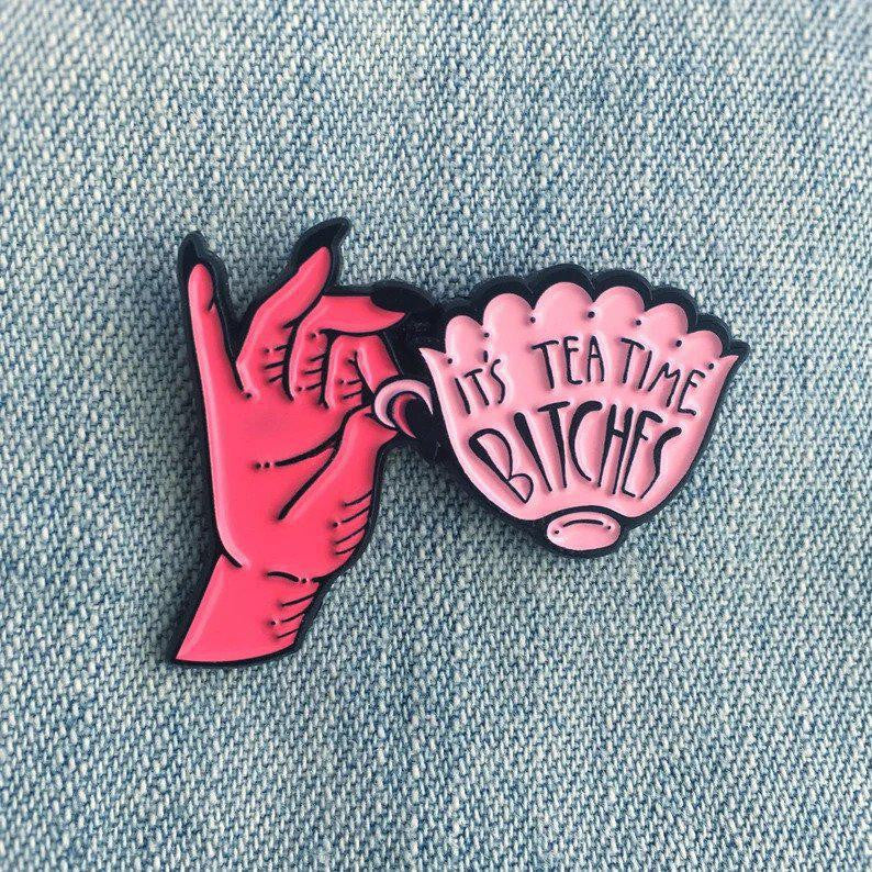 Its Teatime, Bitches enamel pin held in a pink hand.