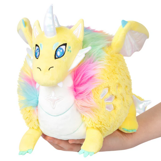 Mini Squishable Prismatic Dragon plush with blue eyes, rainbow fur, wings, and shiny horn held in hands.