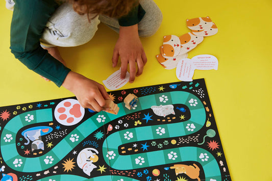 Catventures Board Game with pawns and illustrated cards in use on a yellow surface.