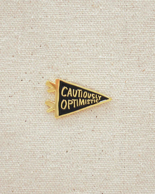 Gold and black enamel Cautiously Optimistic Pin shaped like a pennant.