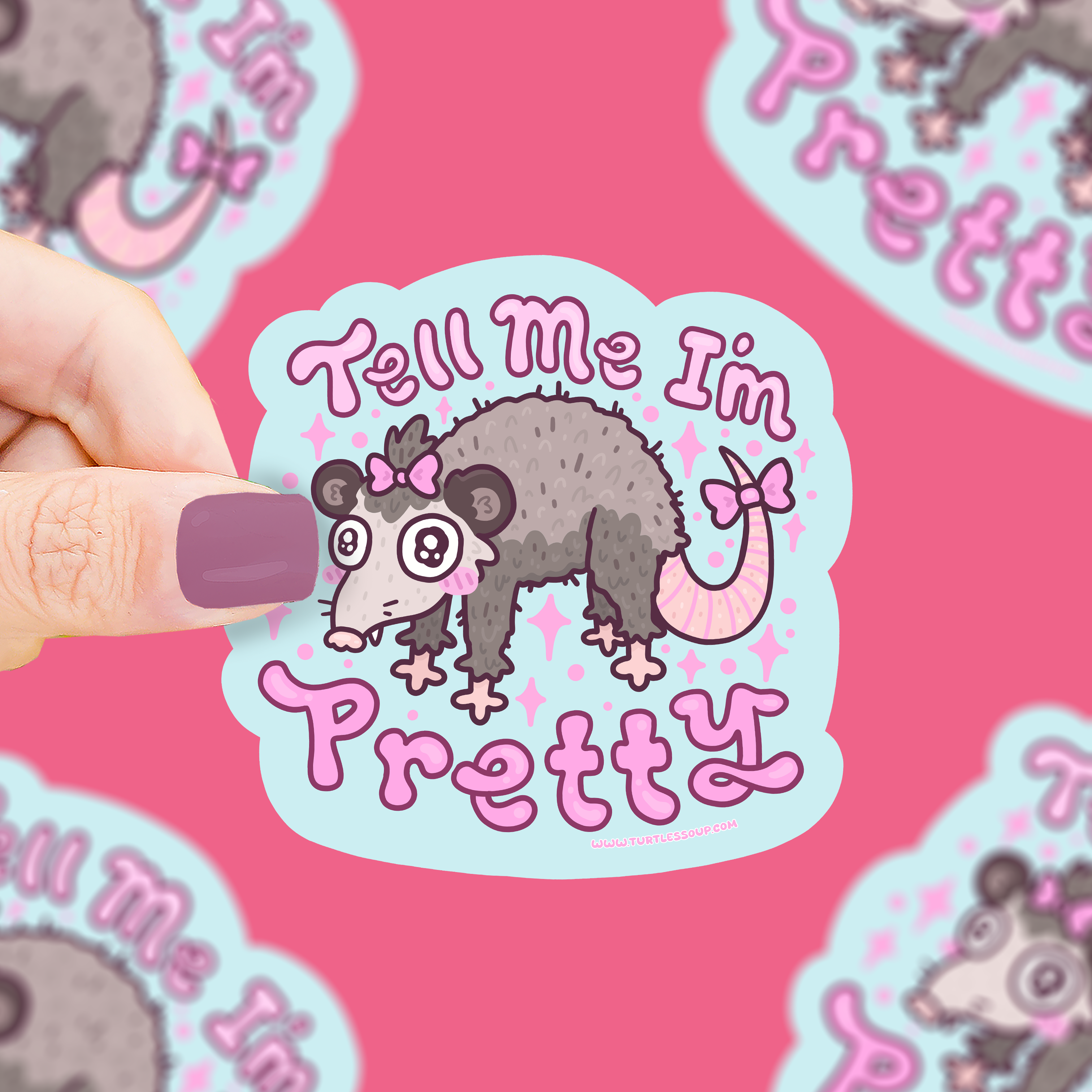 Tell Me I’m Pretty opossum bow vinyl sticker from the Opossum Trash collection held by a hand with purple nails.