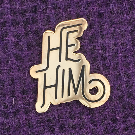 Gold He/Him pronoun lapel pin with bold lettering.