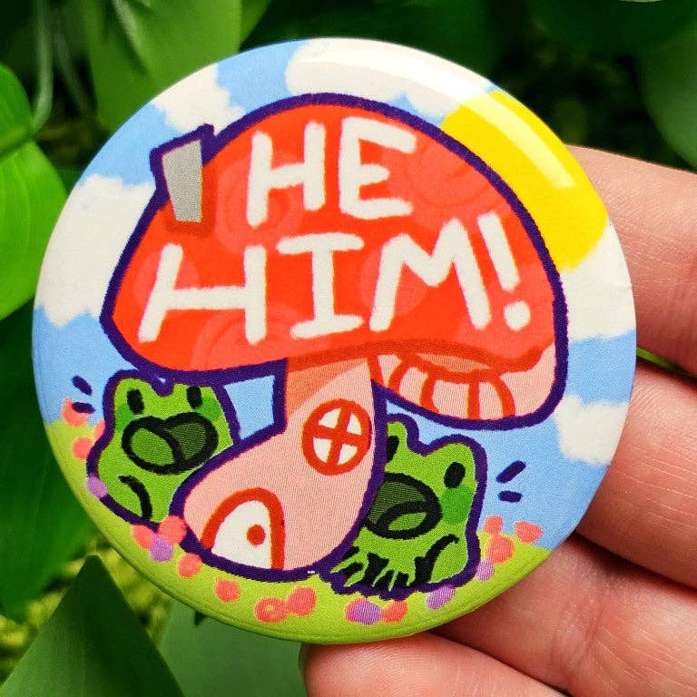 Large waterproof laminated button with He/Him text and frogs on a mushroom house.