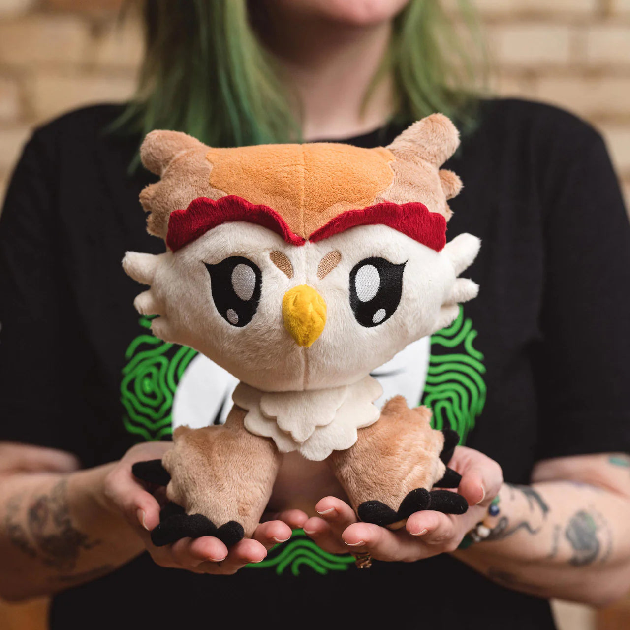 Tattooed person holding Owlbear Dawn 8 inch plushie with big eyes, inspired by TTRPGs.