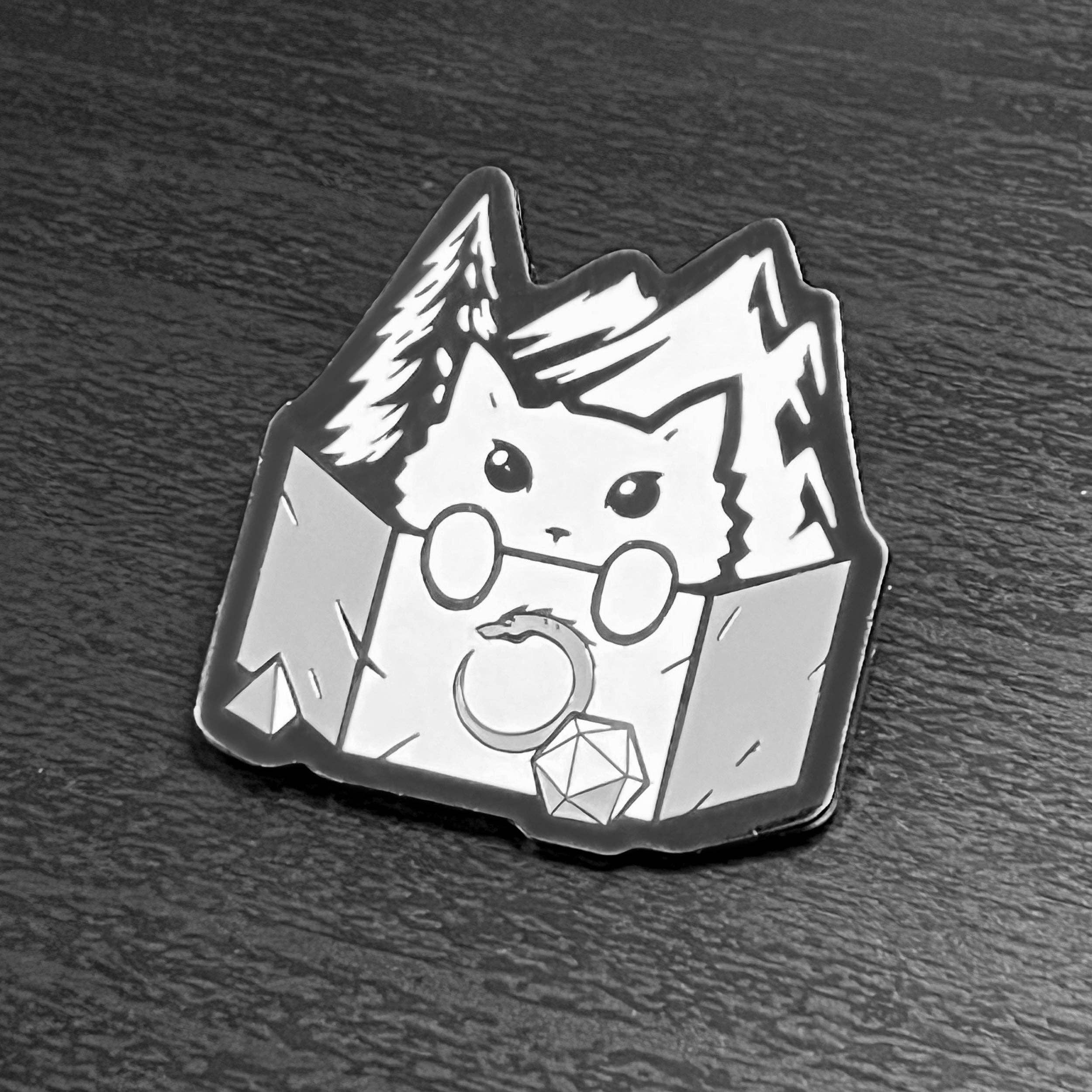 Enamel pin of a cat as DM behind a screen with dice, mountains, and trees; black nickel plating.