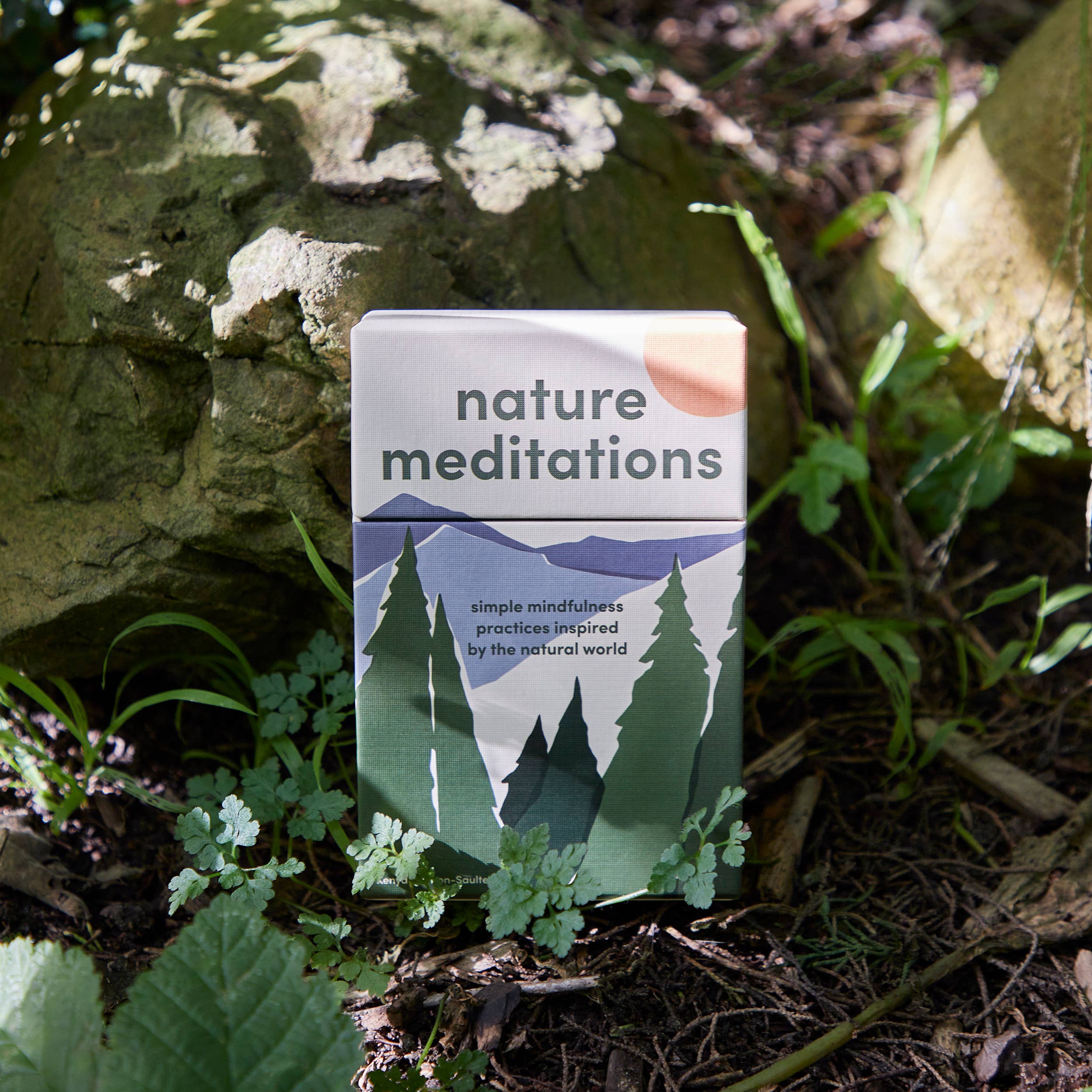 The Nature Meditations Deck displayed outdoors among rocks and plants in sunlight.