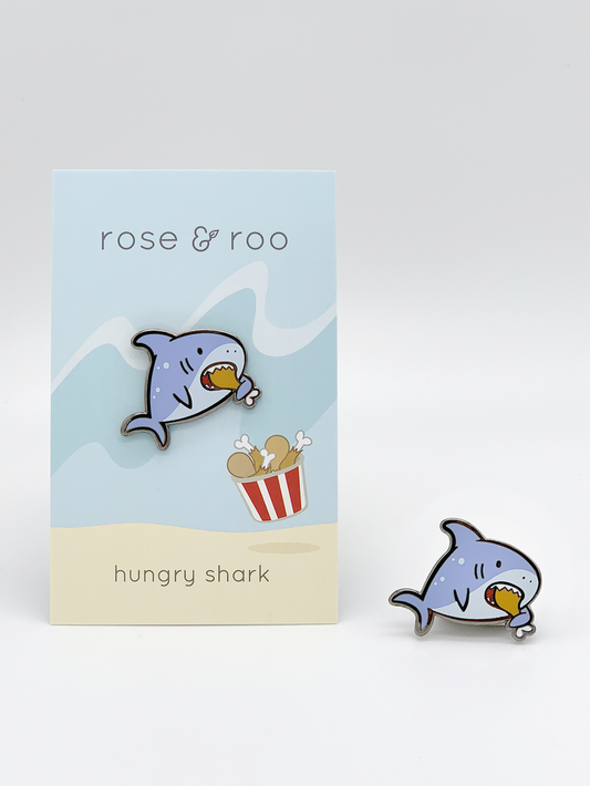 Hungry Shark enamel pin showing a cartoon shark eating chicken, with matching hungry shark card by rose & roo.