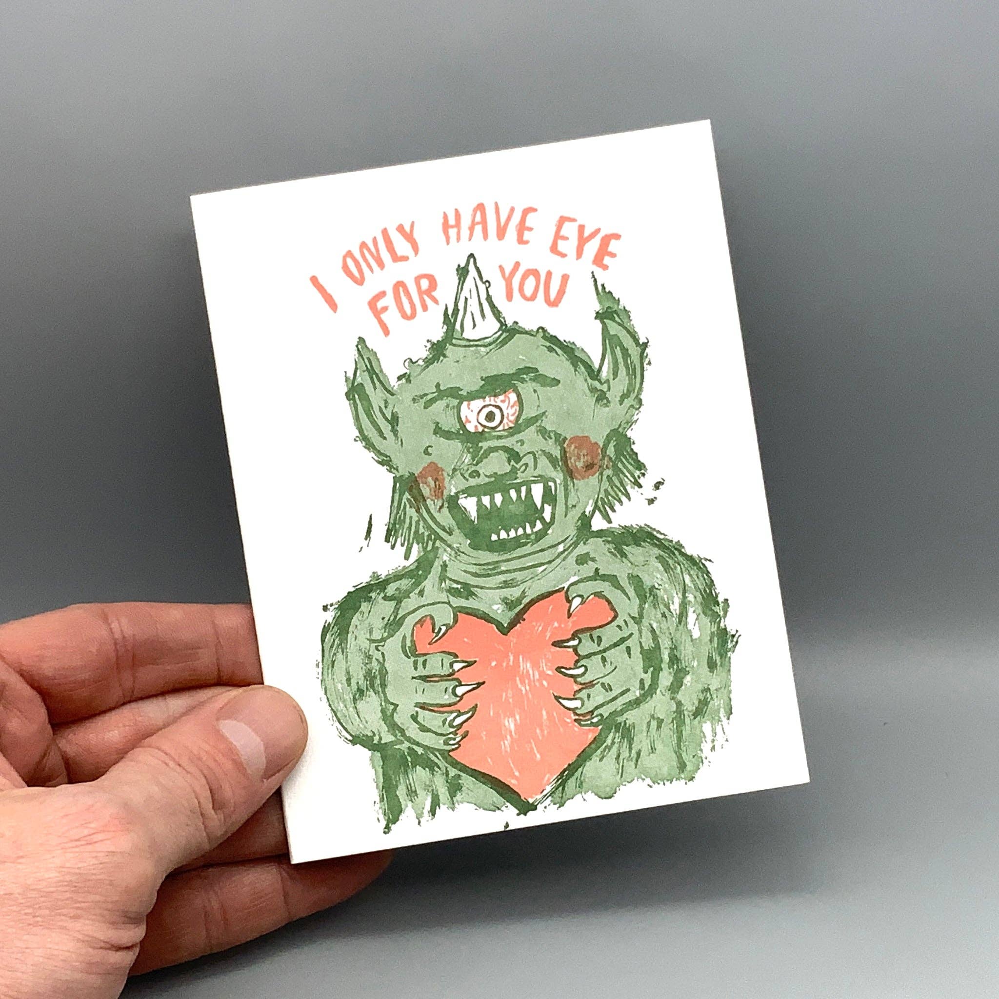 Eye For You letterpress card with green cyclops monster, heart, and caption, held in a hand.