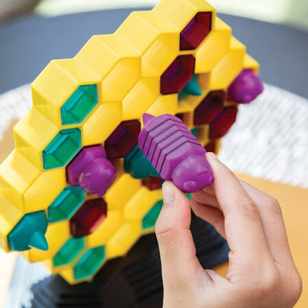 Hand placing a purple bee piece into a yellow board in the Queen Swarm family strategy game.