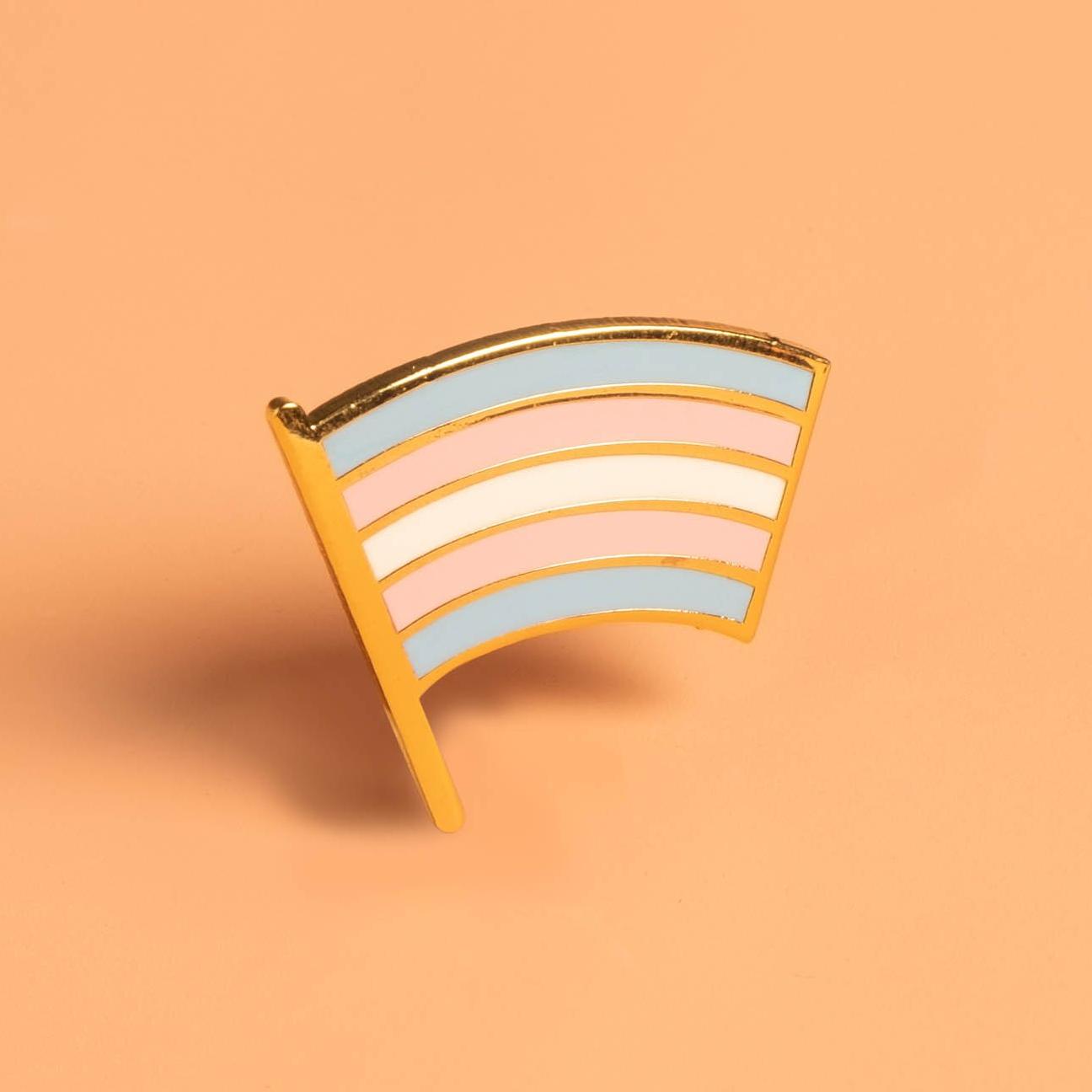 Gold enamel Trans Pride Flag pin with light blue, pink, and white stripes.