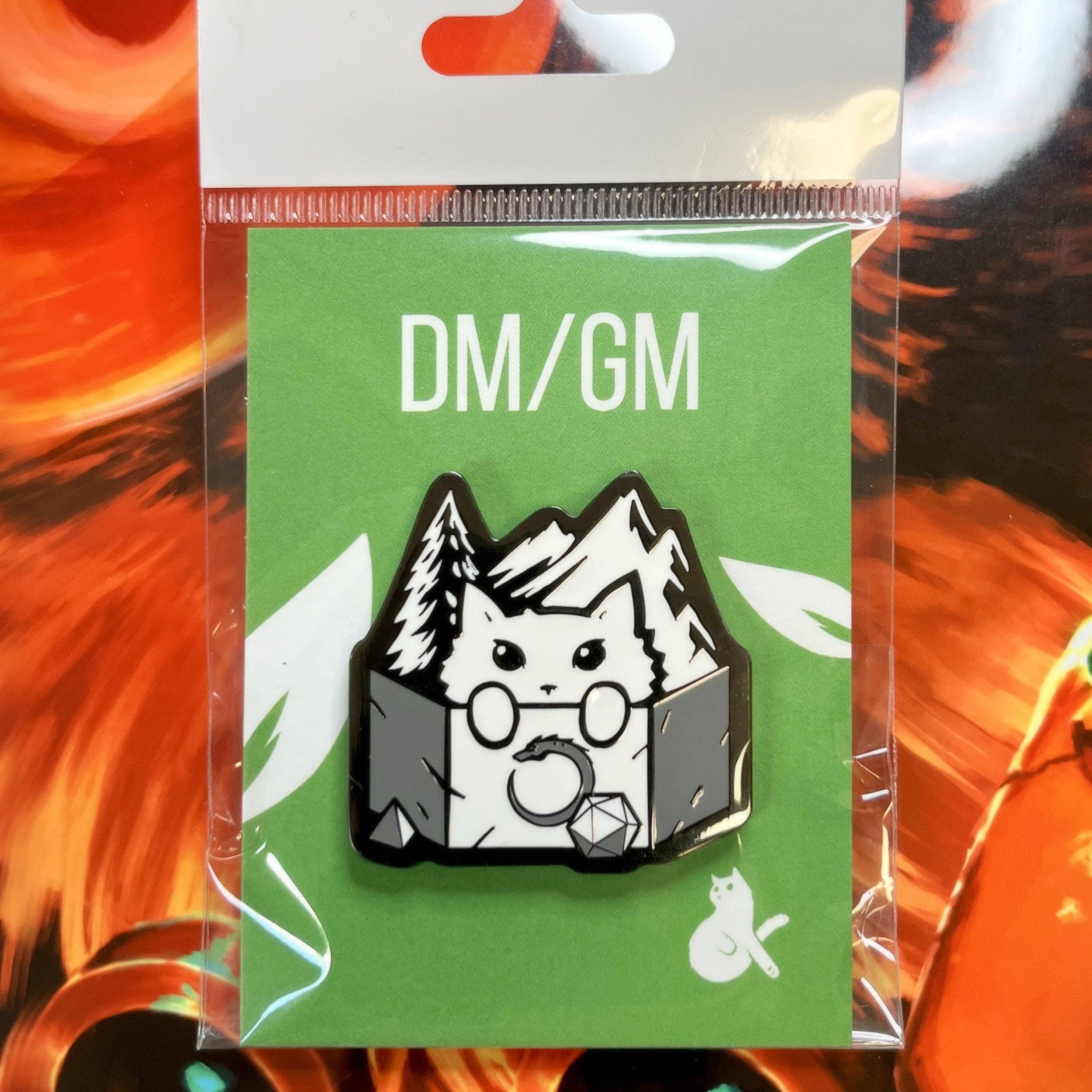 DM/GM enamel pin featuring a cat dungeon master with dice and mountains, black nickel plating.
