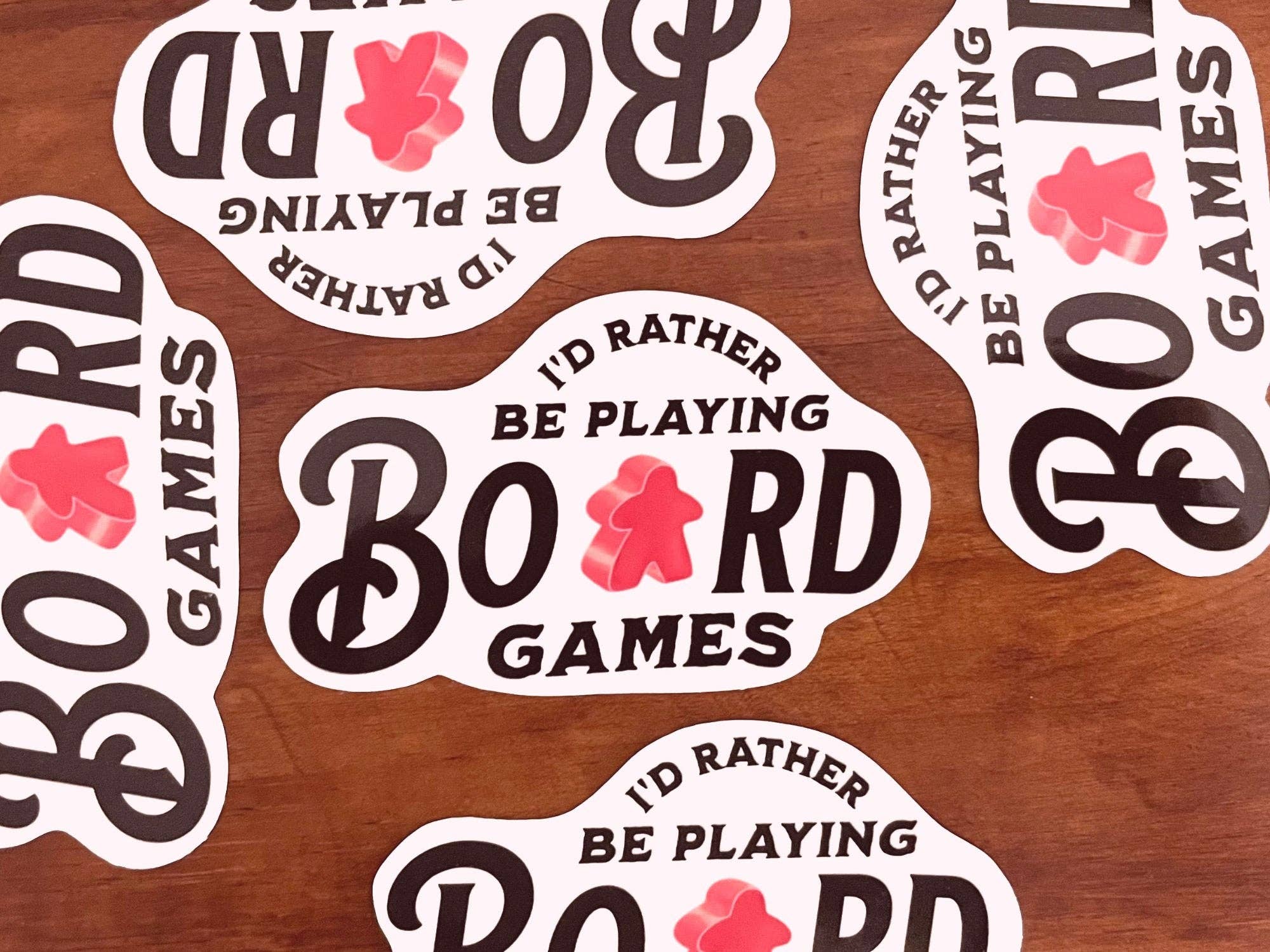 Id Rather Be Playing Board Games sticker with a red meeple on a wood background.
