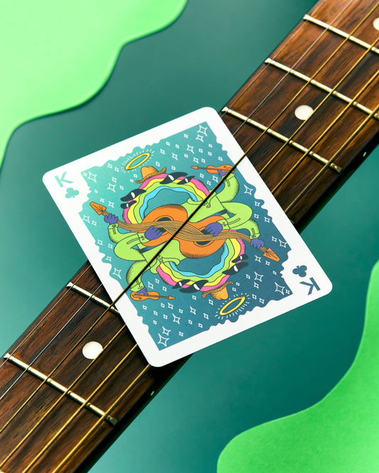 King of clubs playing card from Meow Wolf, featuring a surreal multi-armed figure playing a guitar.