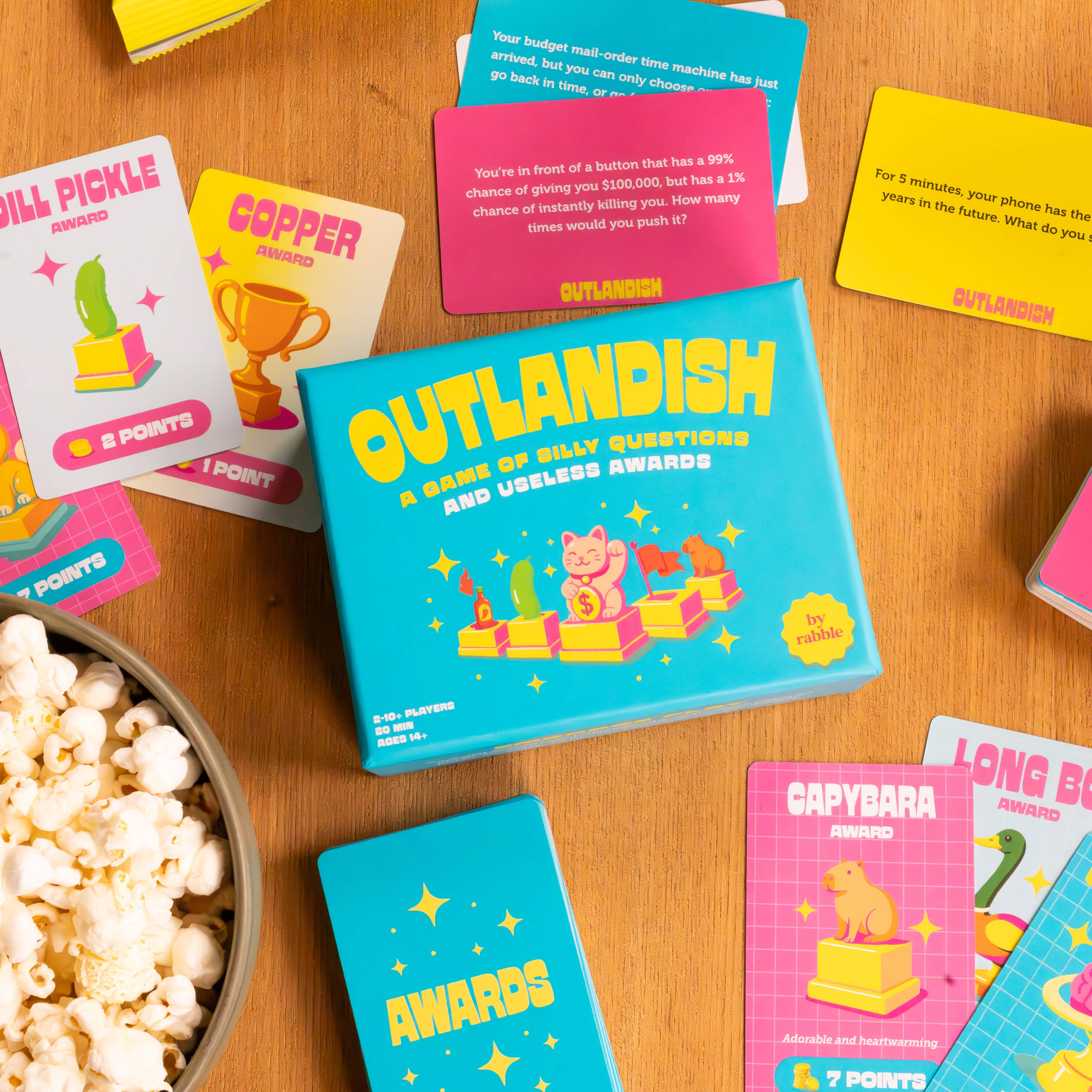 Outlandish board game with cards on a table alongside a bowl of popcorn.