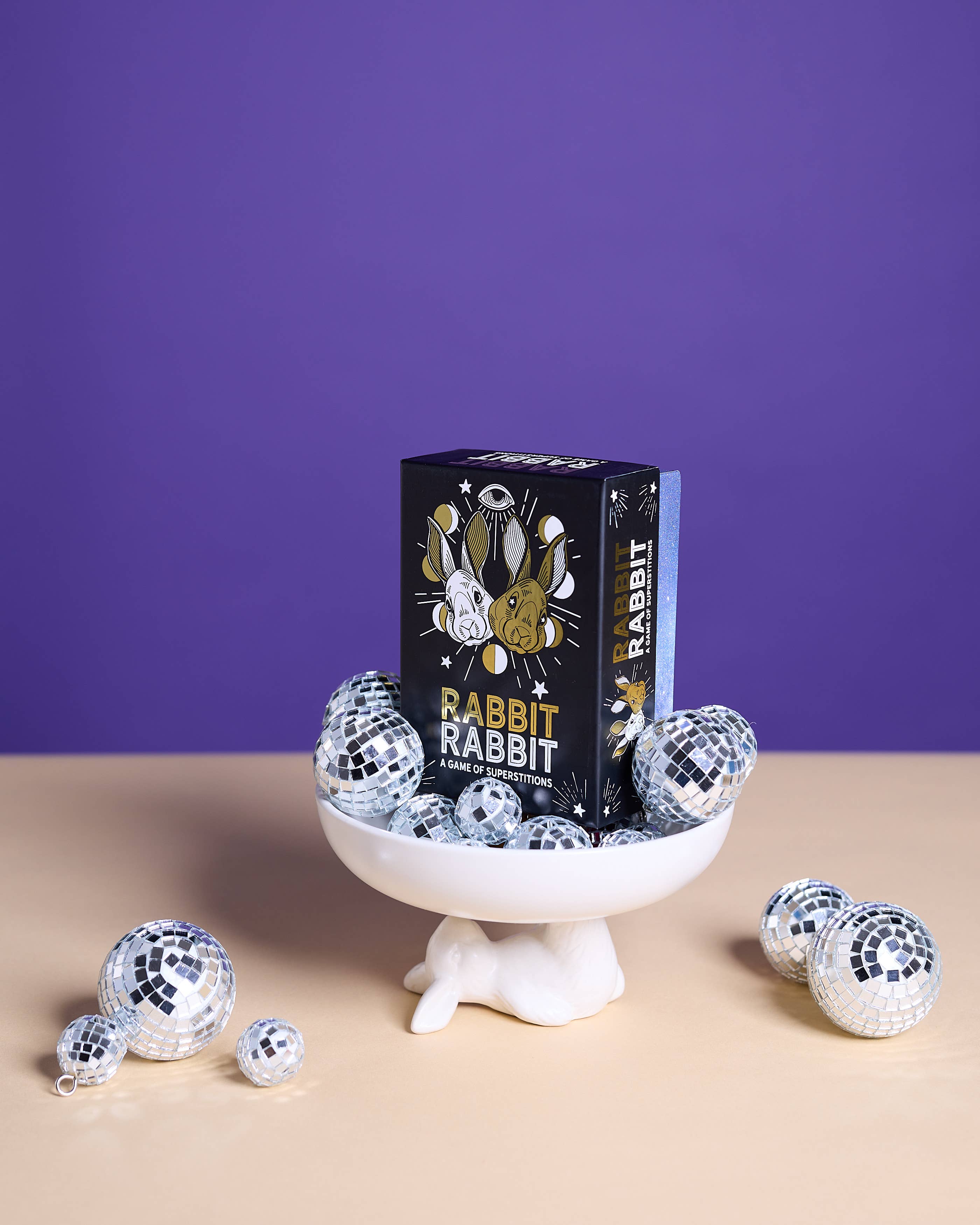 Rabbit Rabbit: A Game of Superstitions box displayed in a rabbit-shaped bowl with disco balls.