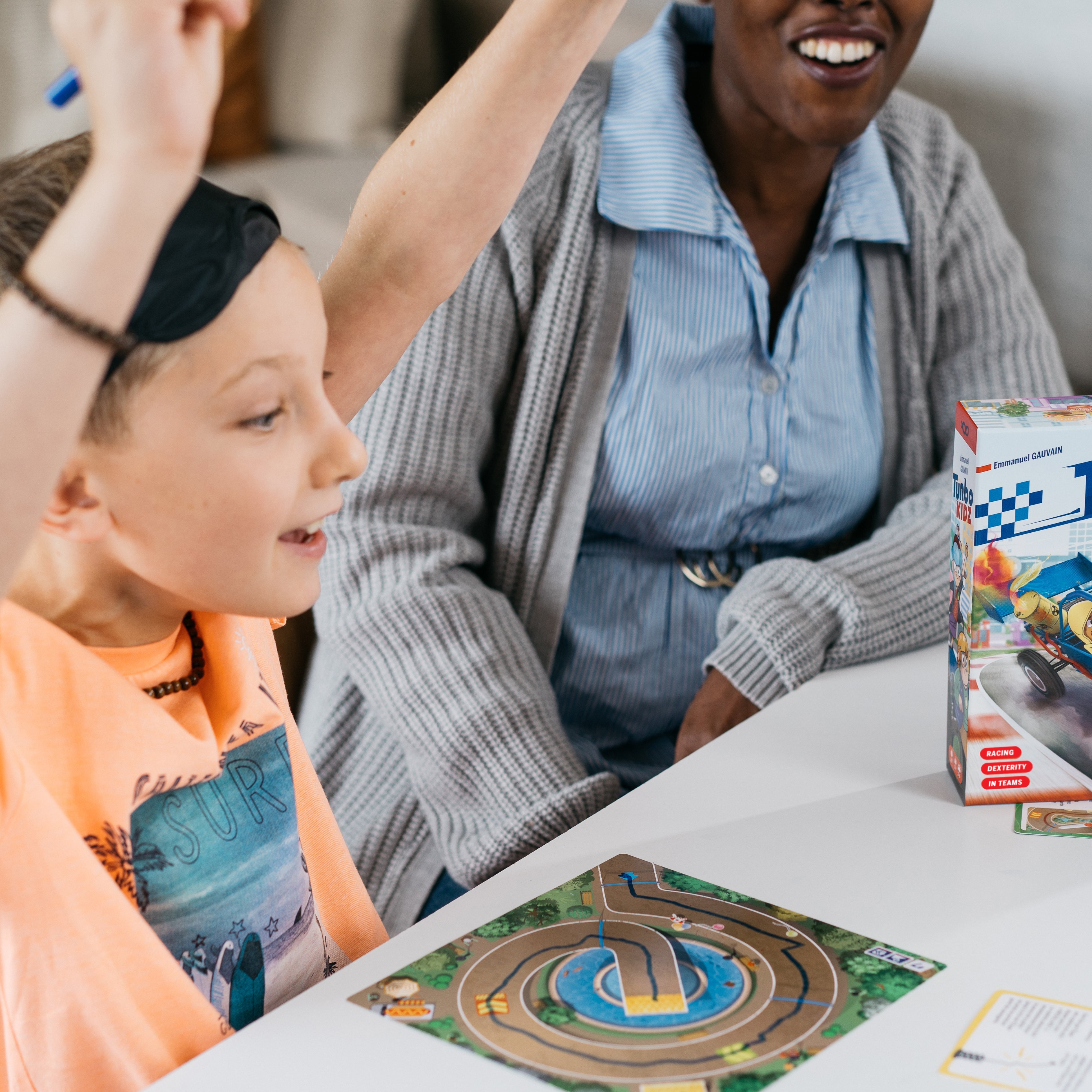 Child plays Turbo Kidz board game at a table, arms raised.