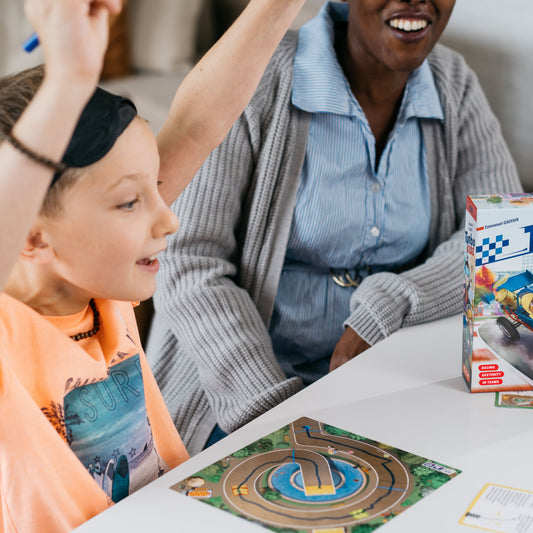 Child plays Turbo Kidz board game at a table, arms raised.