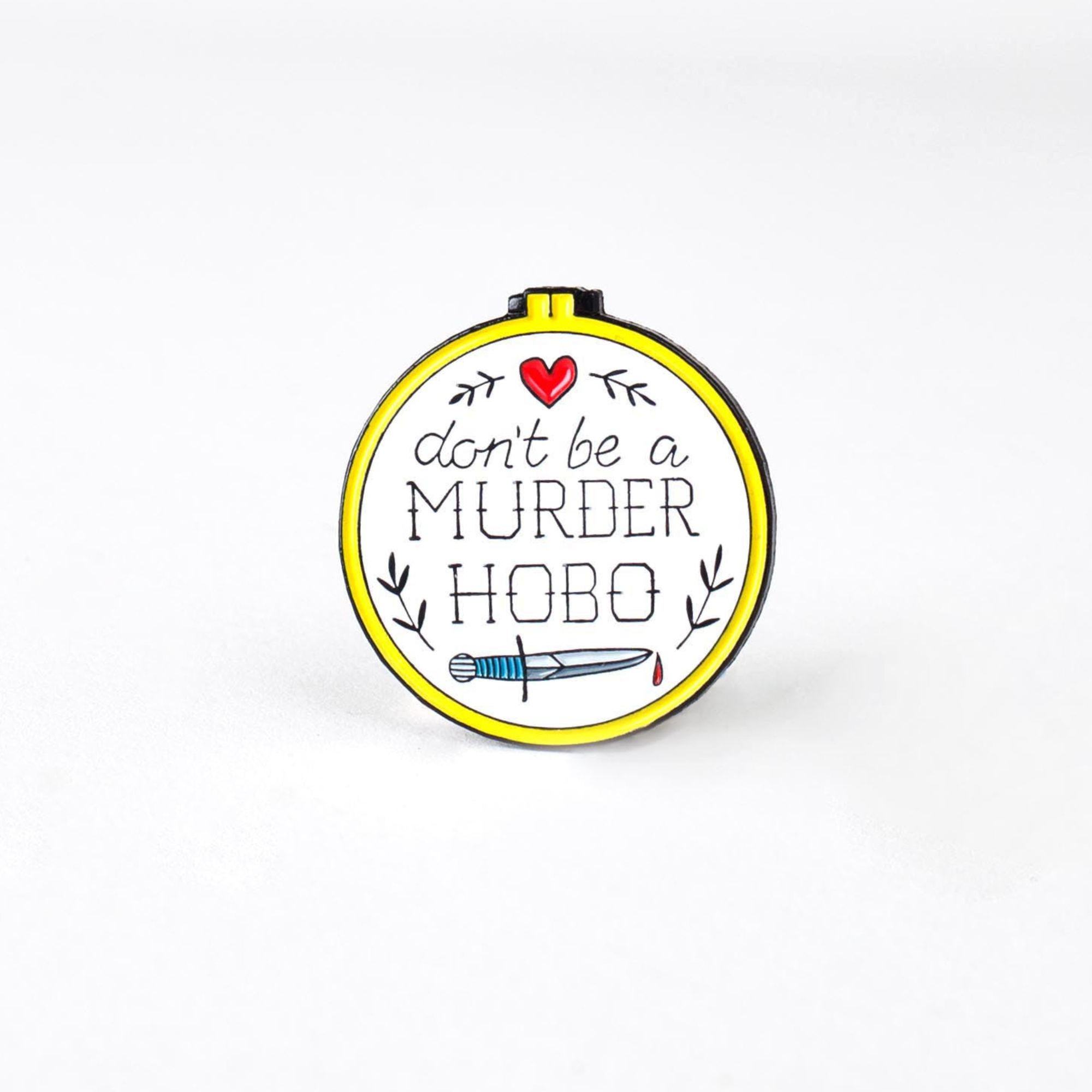 Don’t Be a Murder Hobo enamel pin, round and white, with a heart, branches, and a bloody knife.