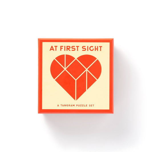 At First Sight Tangram Puzzle by Brass Monkey in a square box with a red heart tangram on the lid.