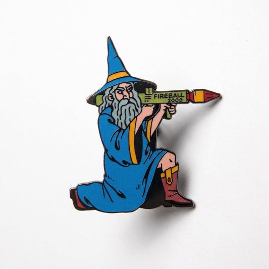 Fireball Wizard enamel pin featuring a wizard in a blue robe firing a black metal rocket launcher labeled FIREBALL 2000.