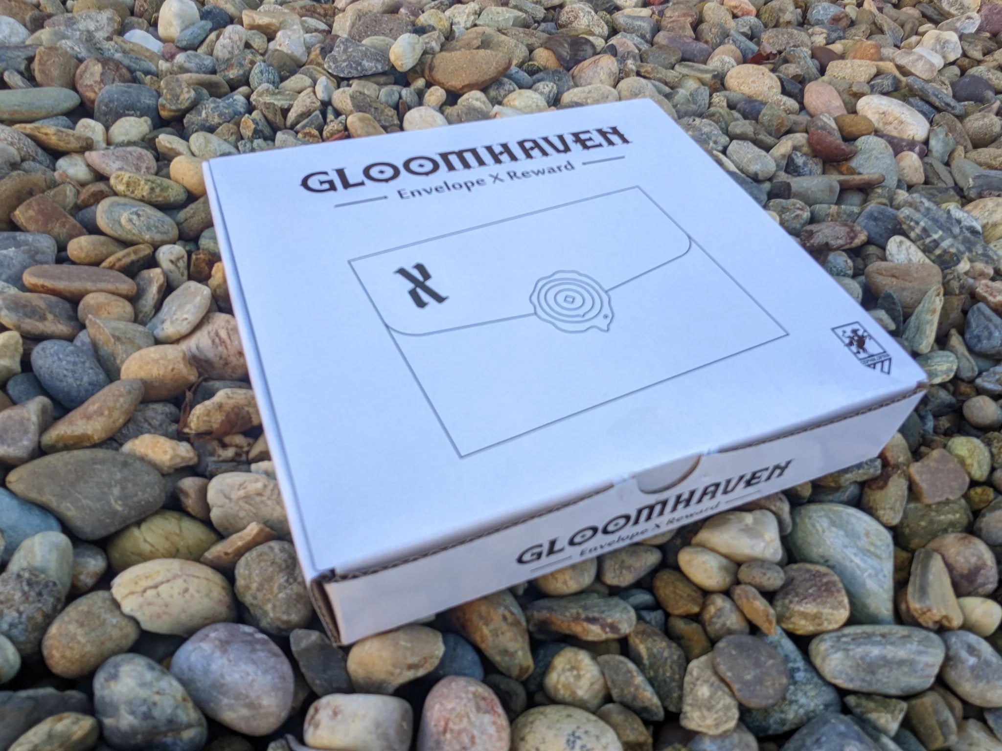 Gloomhaven: Envelope X (1st Edition) box displayed outdoors on rocks.