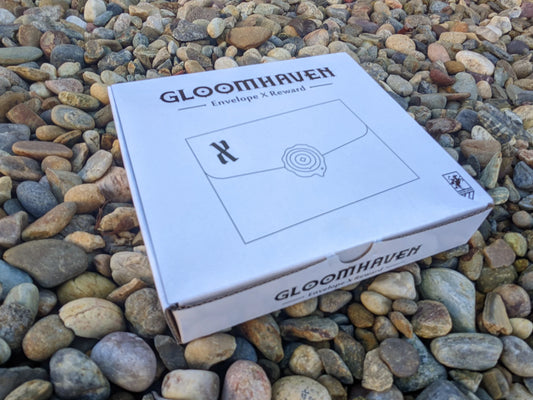 Gloomhaven: Envelope X (1st Edition) box displayed outdoors on rocks.
