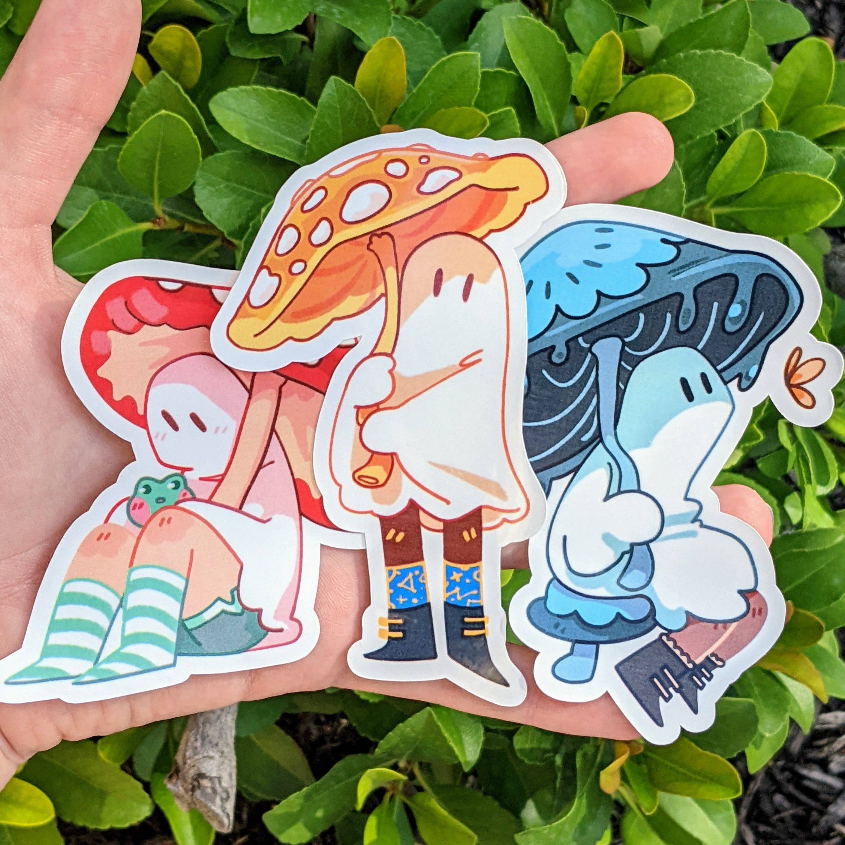 Three Cute Ghost Stickers, V6 variant with cartoon mushroom ghosts, held in a hand.
