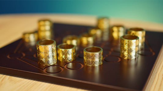 Gold cylindrical playing pieces with engraved patterns on a board for the abstract strategy game Gygѐs.