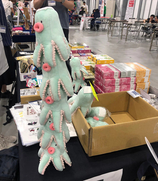 Hexakun Plush, tall light green sea creature with multiple tentacles, displayed on a vendor table.