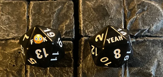 Two black F*ck Yeah D20 dice featuring emoji and OK/YEAH in place of numbers.